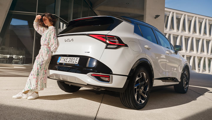 Kia EV9 GT, Nahaufnahme Scheinwerfer Fahrerseite, Frau lehnt an Fahrzeug