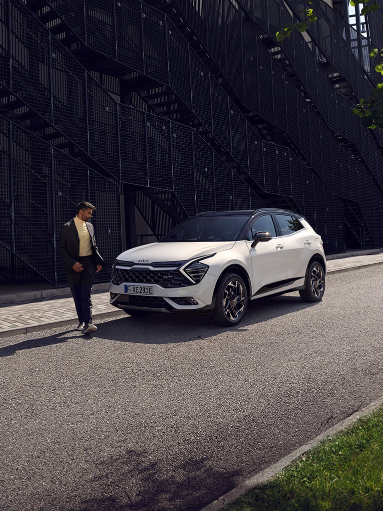 Kia Sportage Plug-in Hybrid, weiß, Seitenansicht Fahrerseite, Mann läuft vor dem Auto über die Straße