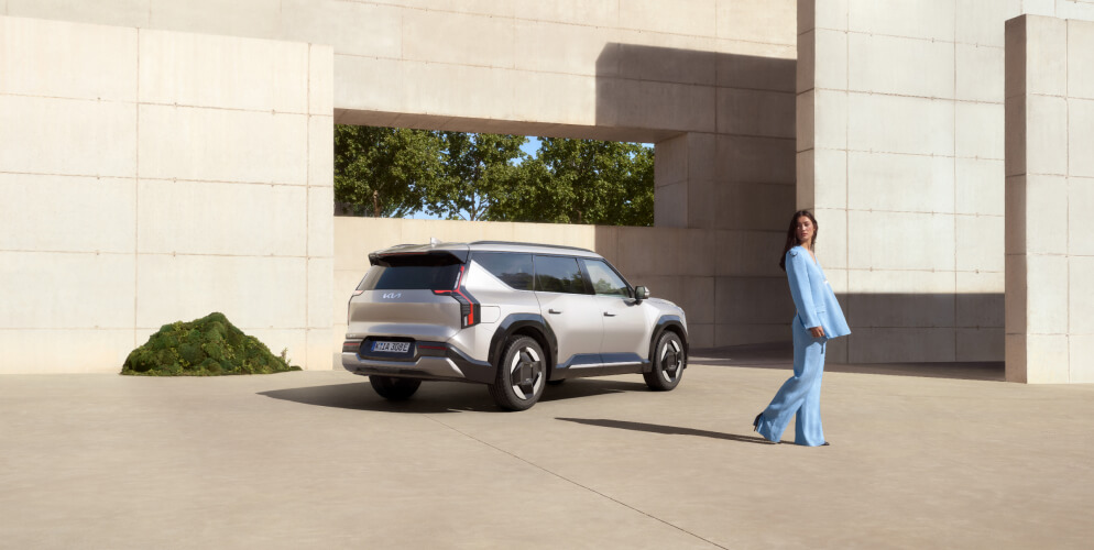 Eine Frau steht vor einem Kia EV9 in Heckansicht.